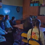 Uczestnicy seansu filmowego siedzą na krzesłach i kanapie i oglądają film. Przed uczniami stoi stół, a na nim znajdują się przekąski (popcorn, ciastka, chrupki) oraz picie.