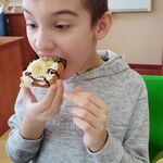 Uczeń odgryza kawałek gofra z bitą śmietaną, polewą  owocami.