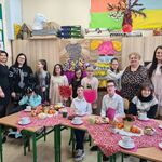 Nauczycielki i uczniowie na tle stolików zastawionych słodkościami.
