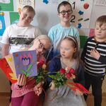 Chłopcy stoją za dziewczynkami, które trzymają laurki i kwiaty.