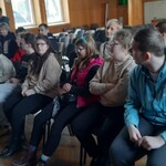 Grupa uczniów siedzi na krzesłach w auli.