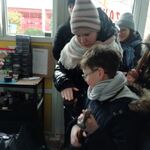 Uczennica trzyma szczotkę do czyszczenia butów, chłopiec młotek szewski,