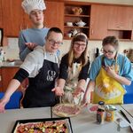 Czwórka uczniów wskazuje ręką pizzę stojąca przed nimi na stole.
