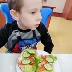 Przed uczniem stoi talerz z kanapkami z pomidorami, sałatą i ogórkiem.