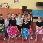 Grupa dzieci. W pierwszym rzędzie dziewczynki w kolorowych spódnicach w grochy.