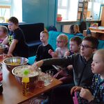 Uczestnicy seansu filmowego, którzy siedzą na krzesłach i kanapie. Przed uczniami stoi stół, a na nim znajdują się przekąski (popcorn, ciastka, chrupki) oraz picie.