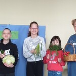 Uczeń trzyma w rękach kapustę, Obok stoją uczennice z koperkiem i cebulą w dłoniach oraz nauczycielka z koszykiem.