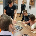 Uczniowie siedzą przy stole. Pani prowadząca omawia pracę warsztatową.