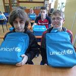 Uczniowie siedzą w ławkach. Przed nimi leżą plecaki z UNICEF-u.