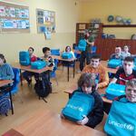 Uczniowie siedzą w ławkach. Przed nimi leżą plecaki z UNICEF-u.