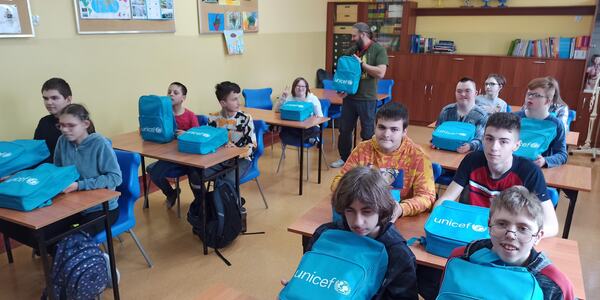 Uczniowie siedzą w ławkach. Przed nimi leżą plecaki z UNICEF-u.