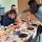 Trójka uczniów siedzi przy urodzinowym stole. Nauczycielka zapala świeczki na torcie.