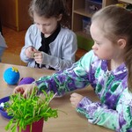 Dziewczynki siedzą przy stole i ozdabiają jajka styropianowe.