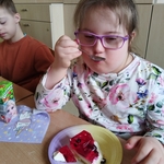 Dziewczynka w różowych okularach je tort z czerwoną galaretką i owocami
