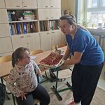 Dziewczynka siedzi na krzesełku. obok stoi nauczycielka z tortem.
