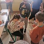 Dziewczynka siedzi na krzesełku i ogląda książeczkę. Wokół niej stoją uczniowie.