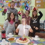 Nauczycielka, jubilat i uczniowie z klasy stoją za urodzinowym stołem.