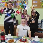 Jubilat siedzi za urodzinowym stołem. Z tyłu stoją koledzy z klasy.