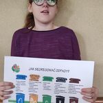 Uczennica prezentuje plakat o segregacji śmieci.