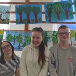 Trójka uczniów na tle prac plastycznych o lesie.