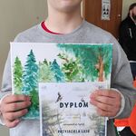 Uczeń prezentuje obraz otrzymany w nagrodę oraz pamiątkowy dyplom za udział w konkursie plastycznym o lesie.