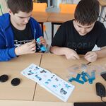 Uczniowie siedzą przy stole i składają robota z  leżących przed nimi elementów.