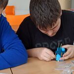 Uczniowie siedzą przy stole i składają robota z leżących przed nimi elementów.