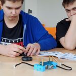 Uczniowie siedzą przy stole i składają robota z leżących przed nimi elementów.
