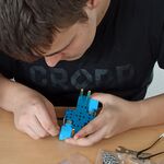 Uczeń siedzi przy stole i składa robota z leżących przed nim elementów.
