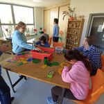 Grupa uczniów układa wzory z dużych kolorowych figur geometrycznych.