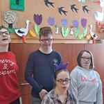 Jubilatka zdmuchuje świeczki na urodzinowym torcie. Z tyłu stoją uczniowie z klasy.