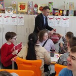 Wiceprezydent Rafał Rudnicki rozdaje uczniom flagi.