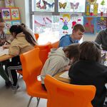 Uczniowie siedzą wokół stołów i malują mazakami plakaty leżące przed nimi.