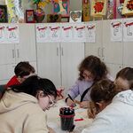 Uczniowie siedzą wokół stołu. Za nimi na szafkach powieszony napis - 2maja święto flagi.