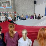 Uczniowie stoją w kółku i trzymają biało-czerwoną flagę w rękach.
