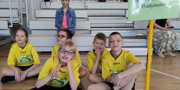 Grupa uczniów siedzi na podłodze przy znaku SP46