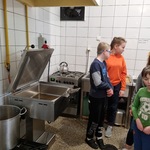 Grupa uczniów stoi obok urządzeń i akcesoriów kuchennych.
