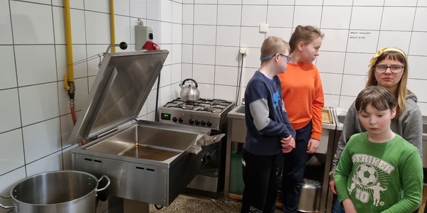 Grupa uczniów stoi obok urządzeń i akcesoriów kuchennych.
