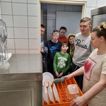 Kucharka stoi przy zmywarce. W tle stoją uczniowie.