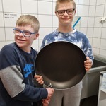 Dwoje uczniów trzyma przed sobą  dużą patelnię.