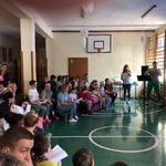 Uczniowie siedzą na ławeczkach i oglądają występ nauczycielek.