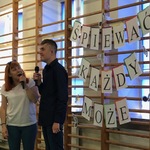 Uczeń i nauczycielka śpiewają do mikrofonów trzymanych w rękach.