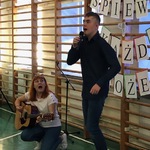 Nauczycielka gra na gitarze. Obok uczeń stoi i śpiewa do mikrofonu.