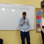 Uczeń recytuje wiersz do mikrofonu. Po bokach stoją nauczycielki.