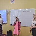 Uczennica mówi do mikrofonu. Obok stoją nauczycielki.