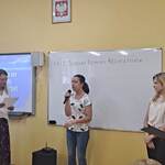 Uczennica mówi wiersz do mikrofonu. Obok stoją nauczycielki.