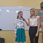 Uczennica mówi wiersz do mikrofonu. Obok stoją nauczycielki.