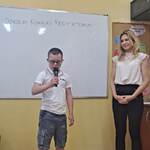 Uczeń mówi wiersz do mikrofonu. Obok stoi nauczycielka.