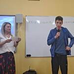 Uczeń mówi wiersz do mikrofonu. Obok stoi nauczycielka.