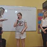 Uczennica mówi wiersz do mikrofonu. Obok stoją nauczycielki.